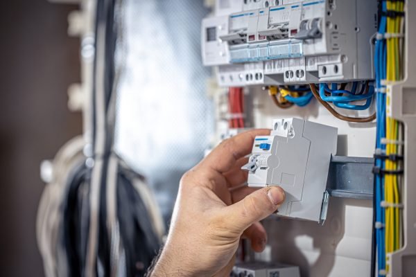 A male electrician works in a switchboard with an electrical connecting cable. Male electrician at the checkout counter on a blurred background of a switchboard.